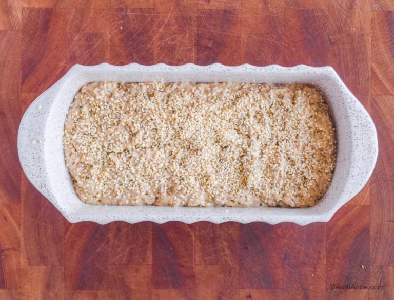 uncooked herb bread in loaf pan with sesame seeds sprinkled on top