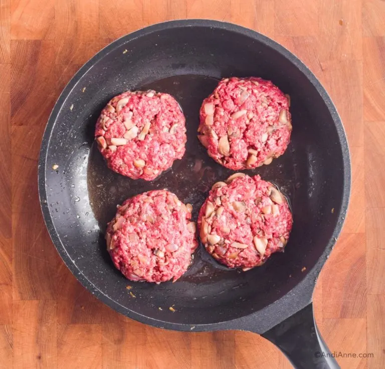 four uncooked mushroom beef patties in a frying pan