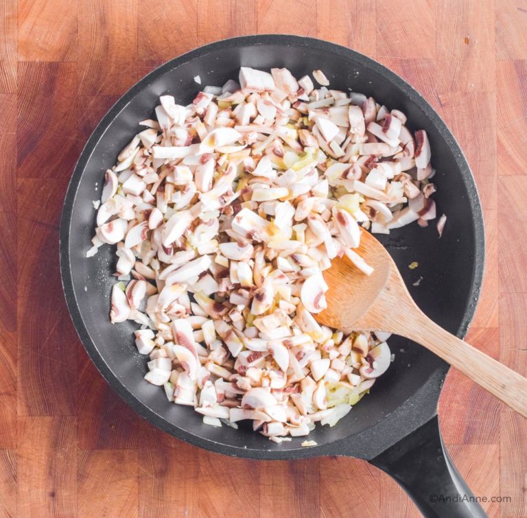 chopped onion and mushrooms in a frying pan with wood spatula