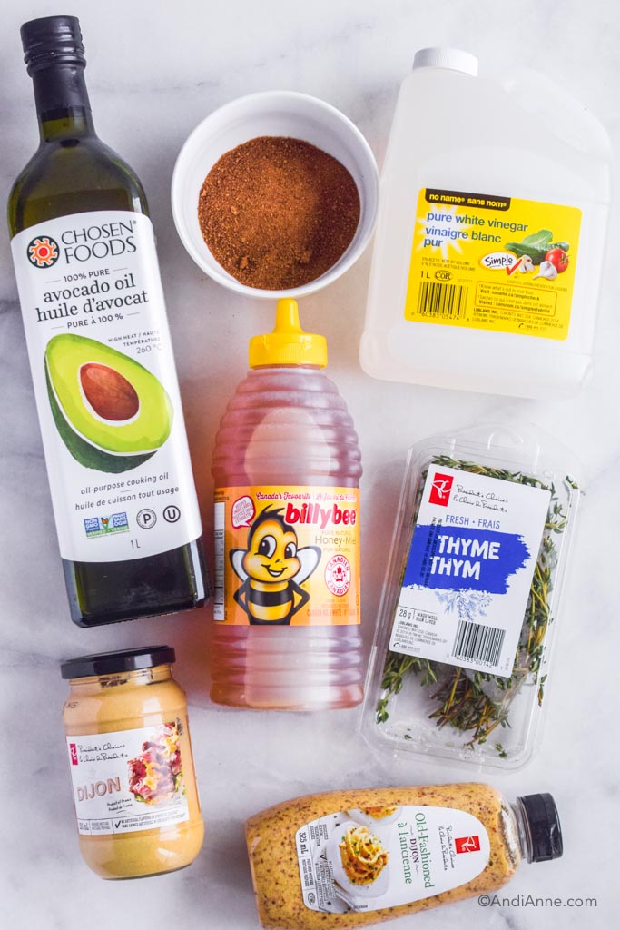 Ingredients to make the glaze laid on the counter: jar of avocado oil, bowl of brown sugar, white vinegar container, liquid honey container, fresh thyme, jar of dijon mustard and container of whole grain mustard. 