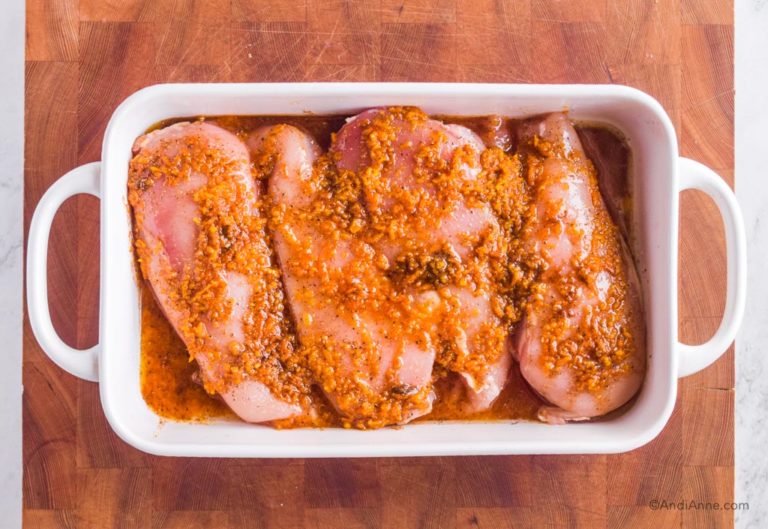 raw chicken breasts with orange sauce poured over top in white baking dish