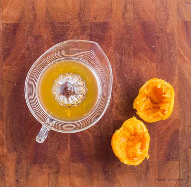 orange juice in glass citrus juicer with two sliced oranges