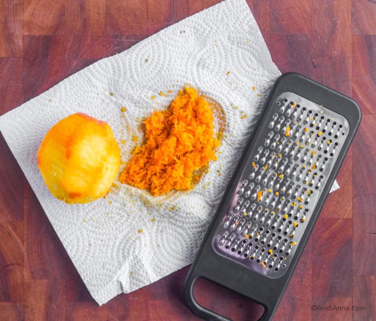 peeled orange, orange zest, grater and paper towel on cutting board