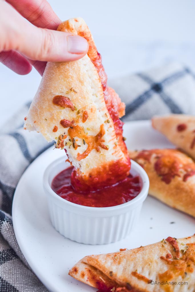 hand dipping in half of pizza pocket into pizza sauce container