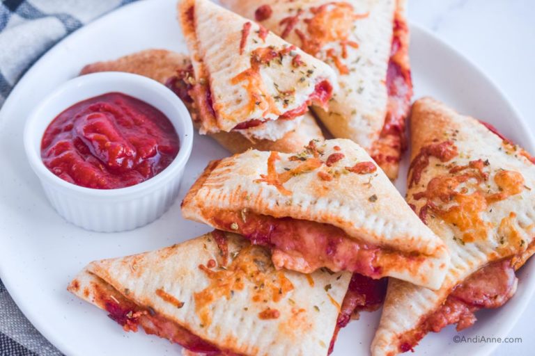 cooked pizza pockets on white plate with small bowl of pizza sauce
