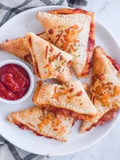 triangled pizza pockets on a white plate with a bowl of pizza sauce.