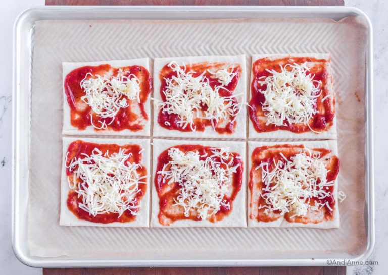six dough squares with pizza sauce and shredded mozzarella on baking sheet