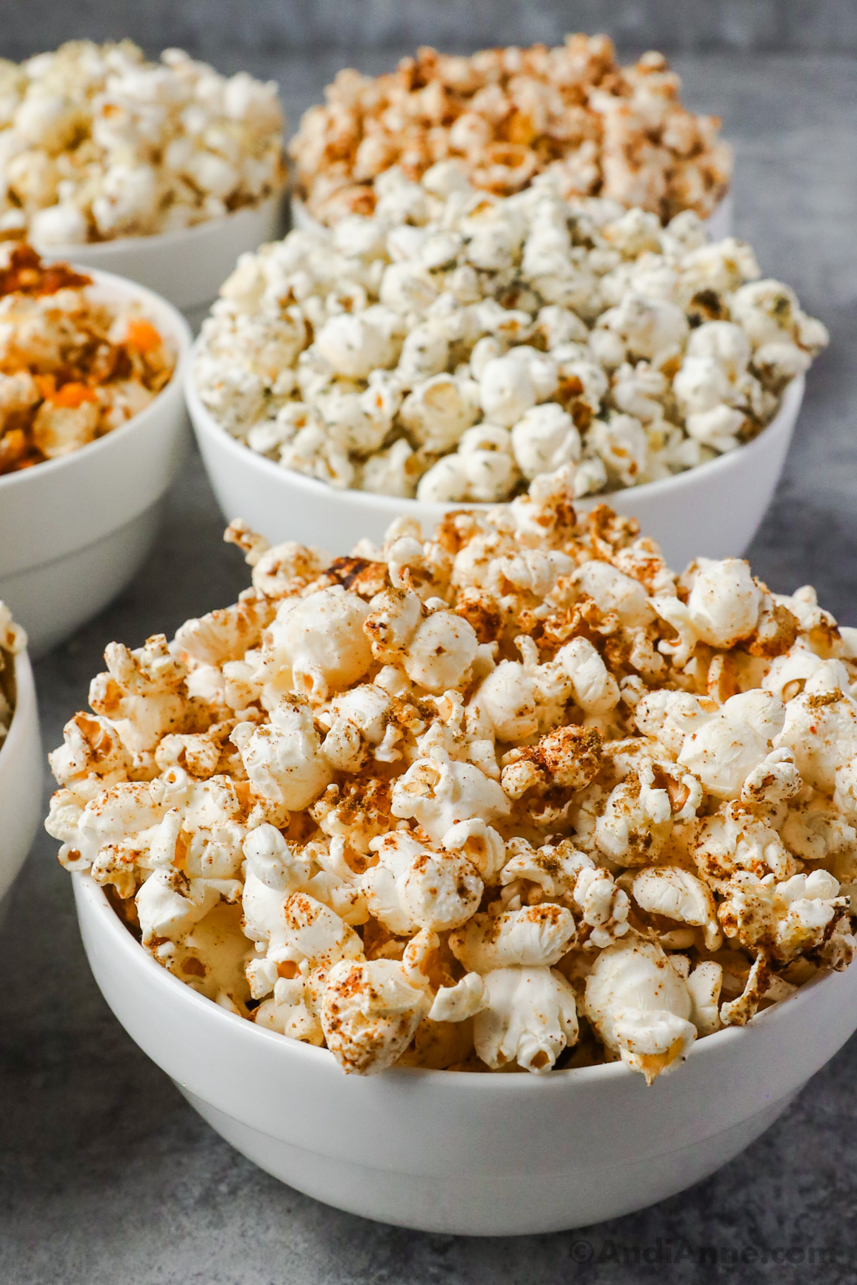 Different bowls of flavored popcorn in rows with the first one close up. 