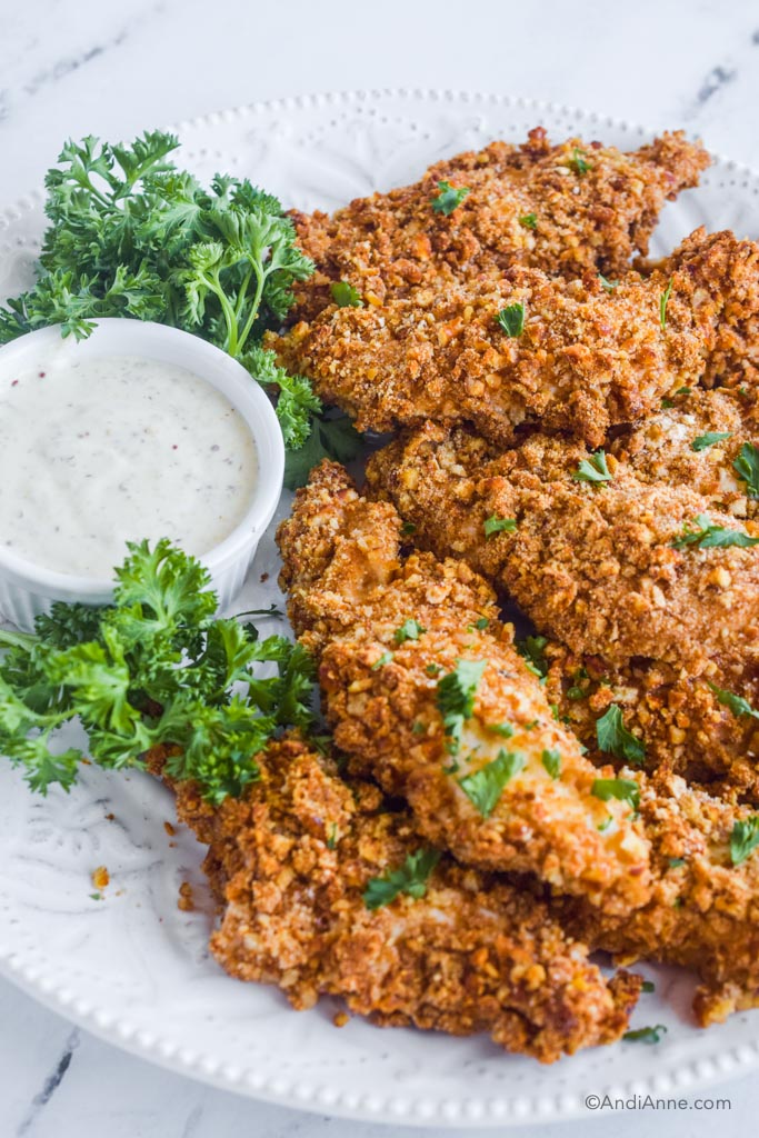 pretzel chicken tenders on plate with dipping sauce and parsley