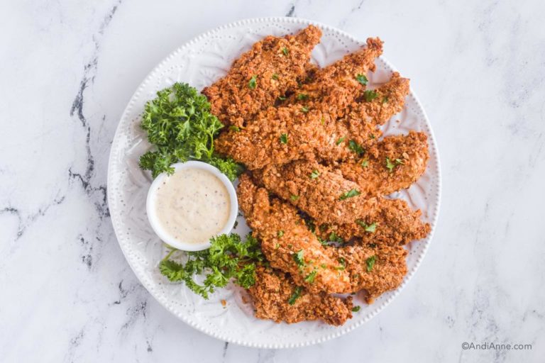 white plate with pretzel chicken tenders, dipping sauce and parsley