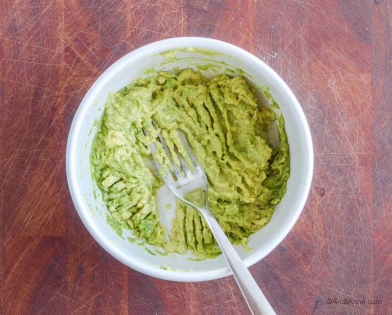 mashed avocado in white bowl with fork