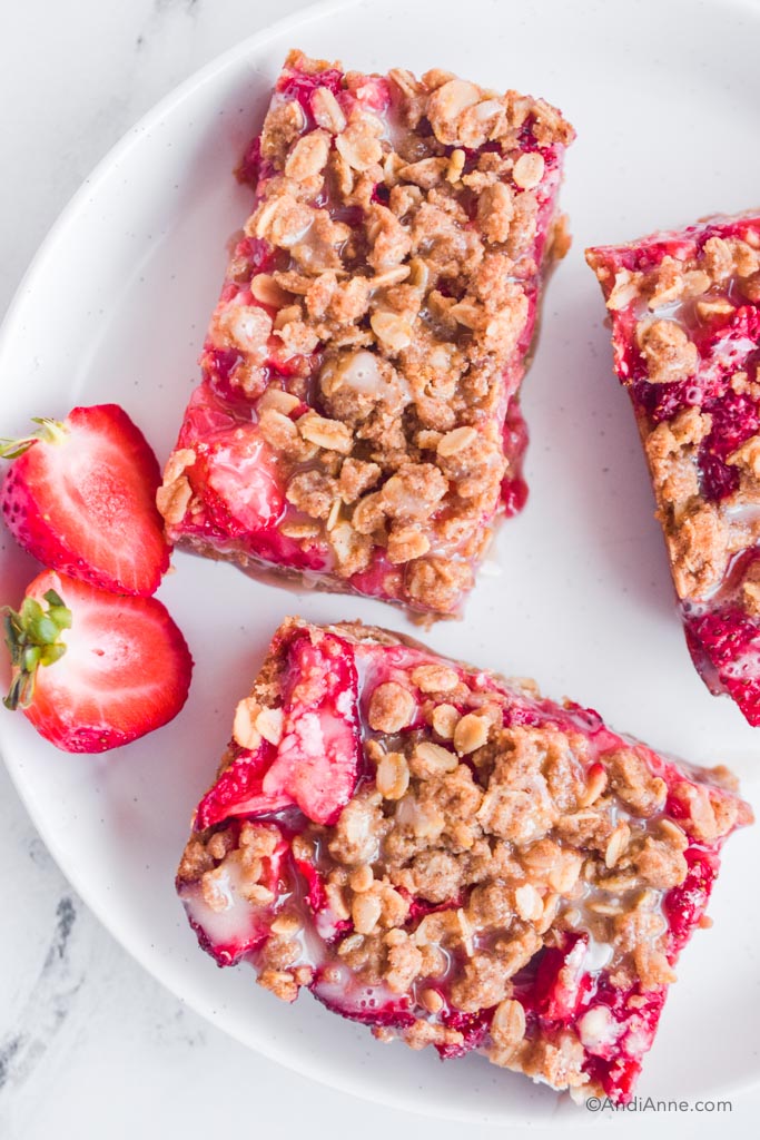 three sliced oatmeal bars on white plate with strawberry sliced in half