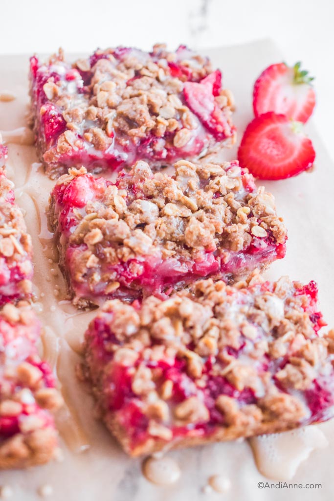 strawberry oatmeal bars on parchment paper with sliced strawberry in background.