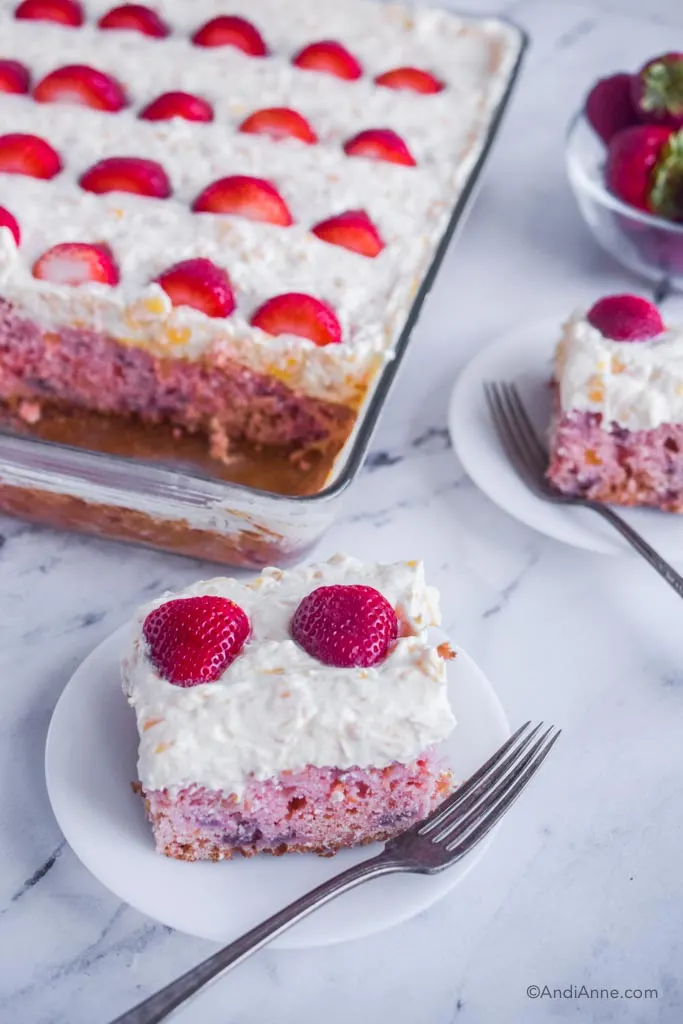 Slices of strawberry pineapple cake on white plates with forks, with glass dish of full cake in background.