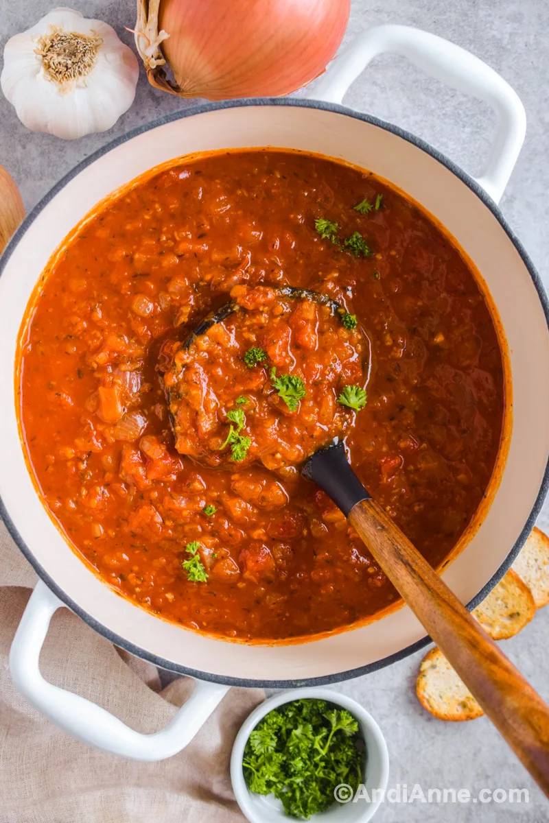 White pot with onion garlic tomato soup and soup ladle inside.