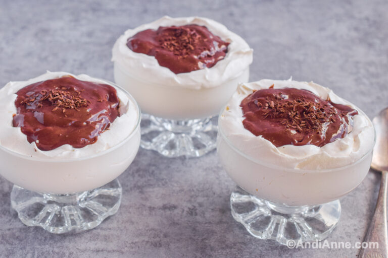 Three glass dessert cups with whipped cream and chocolate pudding in center.