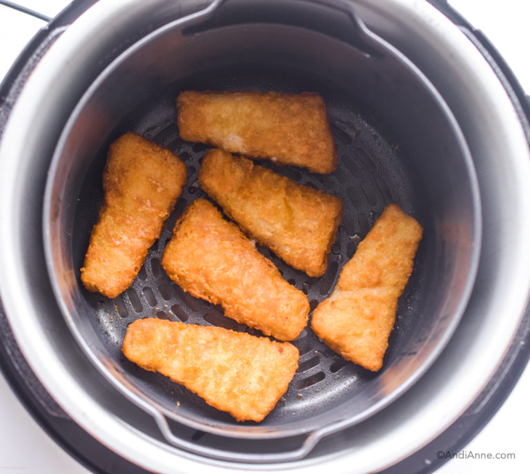 Looking down in an air fryer with 6 fish sticks inside it.