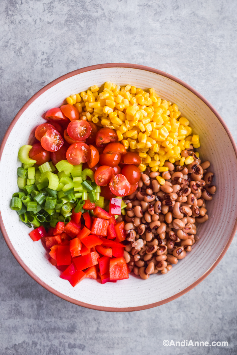 Large white bowl with chopped bell pepper, tomatoes, celery, corn and black eyed peas inside.