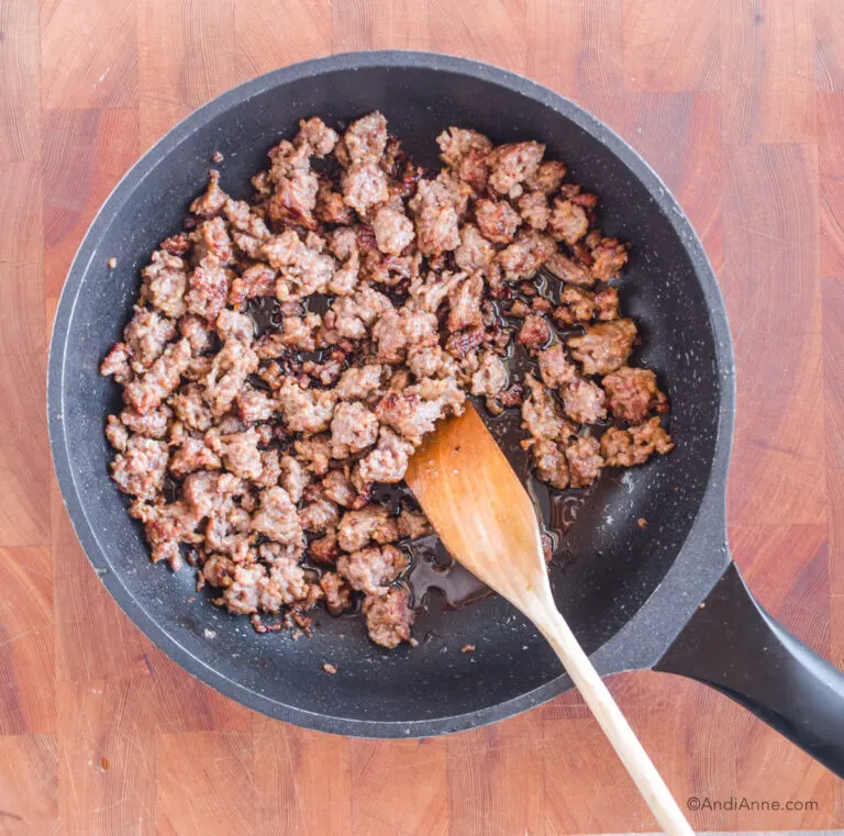 cooked ground sausage meat in frying pan with wood spoon.