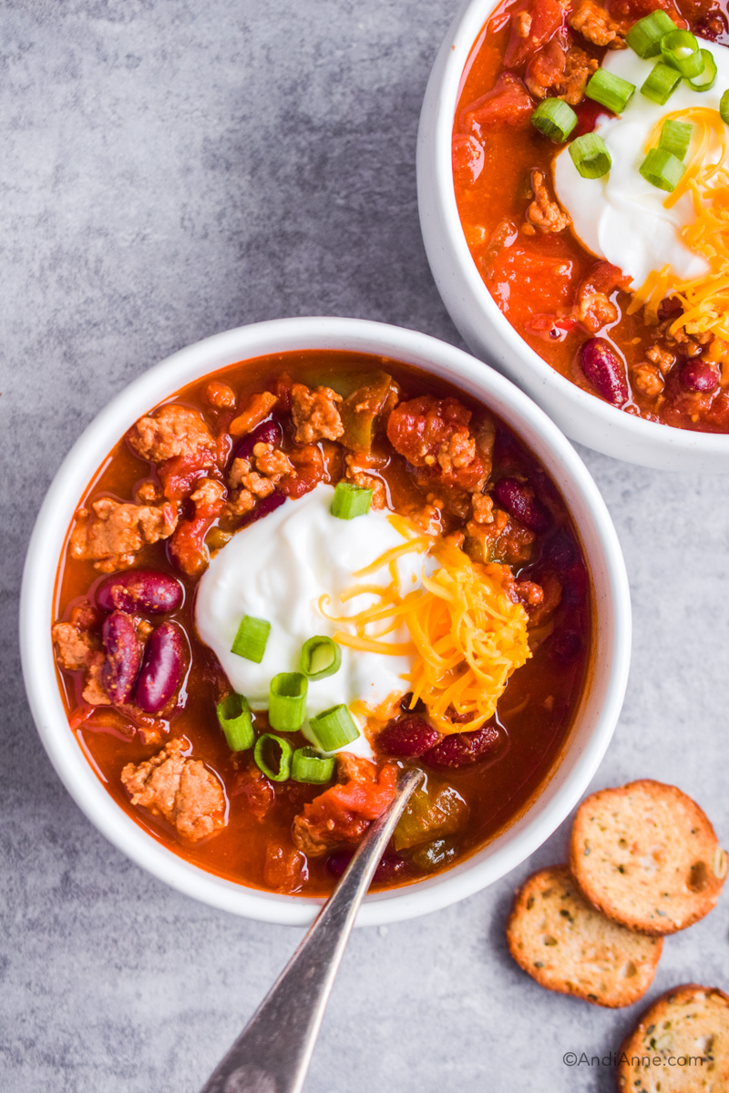 two bowls of instant pot chicken chili with sour cream, shredded cheese and green onion as toppings.