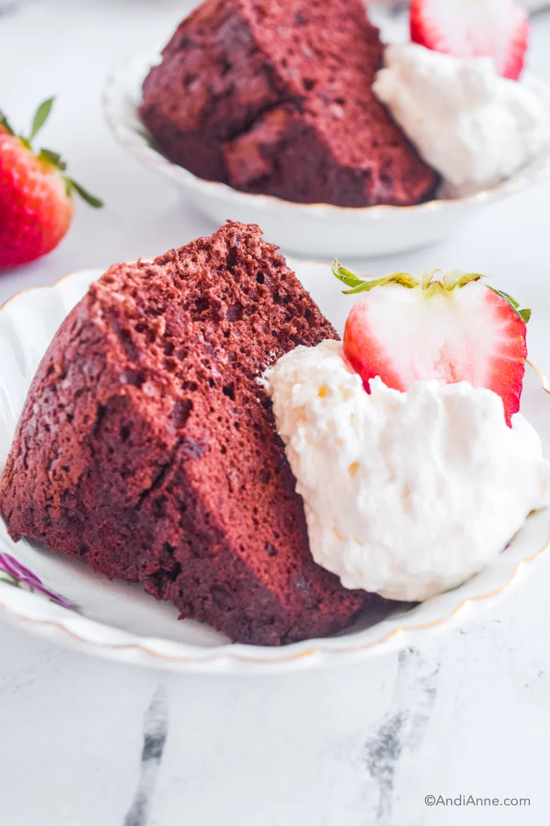 A slice of chocolate angel food cake with a dollop of whipped cream and sliced strawberry. Another serving of cake and a strawberry are blurred in the background.
