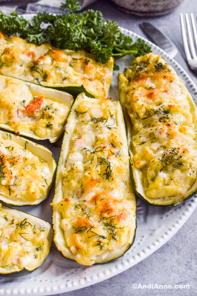 Crab stuffed zucchini on a white plate with fresh parsley and fork in background.
