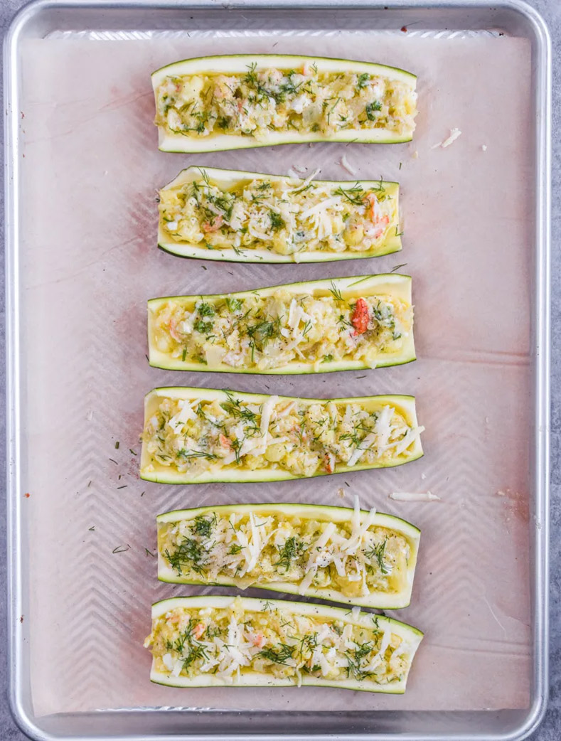 Uncooked zucchini boats stuffed with crab meat filling on baking sheet