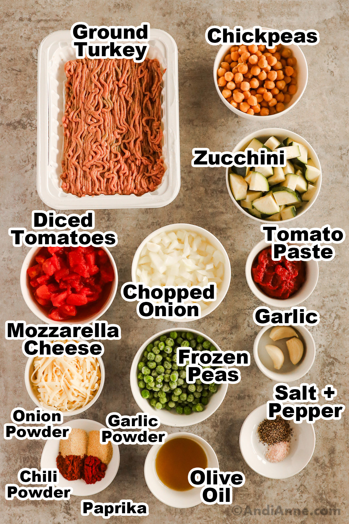 Recipe ingredients including ground turkey, bowl of chickpeas, chopped zucchini, diced tomatoes, chopped onion, tomato paste, shredded mozzarella, frozen peas, garlic cloves, olive oil, salt and pepper, and spices.