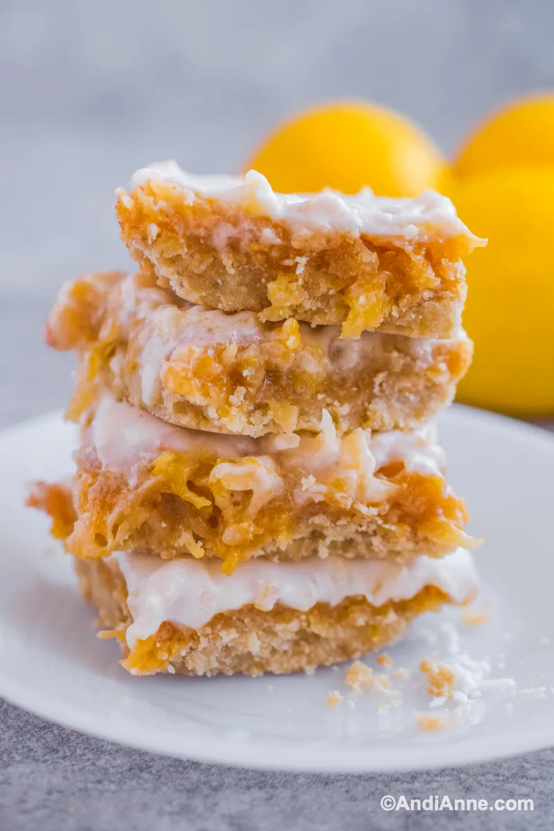 Four lemon coconut squares stacked on top of eachother on a white plate.