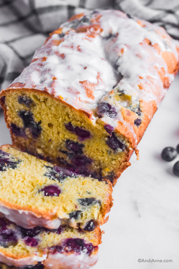 Orange blueberry pound cake with powdered sugar glaze and two slices cut out of it. 