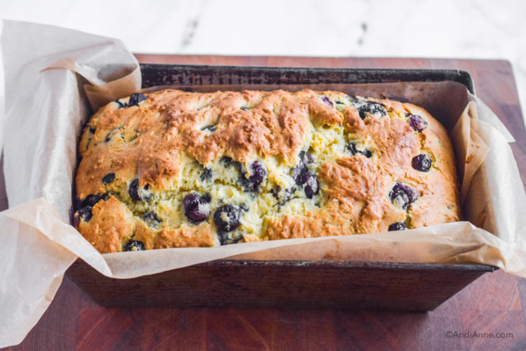 Cooked blueberry pound cake with parchment paper in loaf pan.