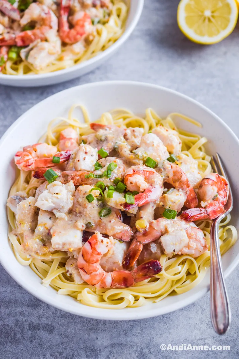 Pasta with shrimp and cod with chopped green onions in a white bowl with a fork. 