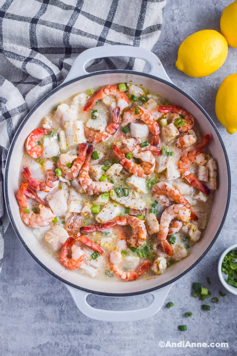 Baked shrimp and cod marinated in a grey cast iron round dish with kitchen towel and lemons surrounding it.