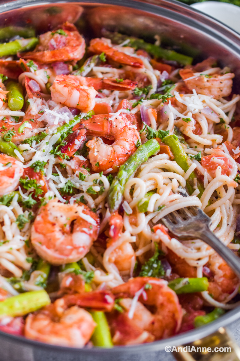 Close up of fork in recipe with noodles, asparagus and shrimp. All sprinkled with grated parmesan.