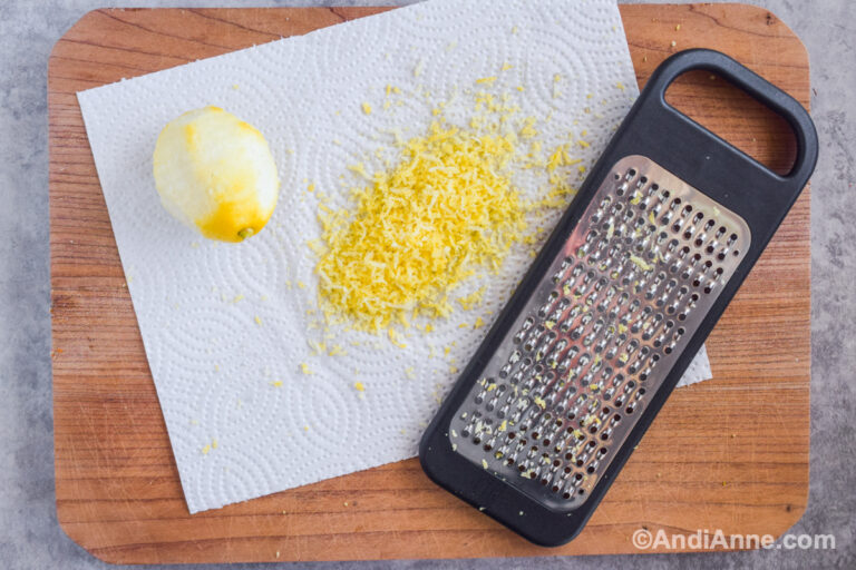 Grated lemon zest, cheese grater and paper towel on a cutting board.