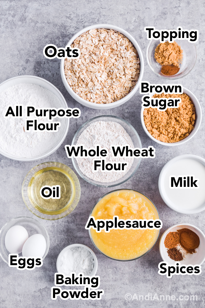 Looking down at recipe ingredients in bowls including rolled oats, flour, brown sugar, applesauce, milk, eggs and oil.