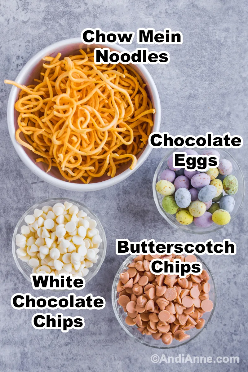 Recipe ingredients in bowls on the countertop including bowl of chow mein noodles, bowl of candy covered chocolate eggs, bowl of white chocolate chips and butterscotch chips.