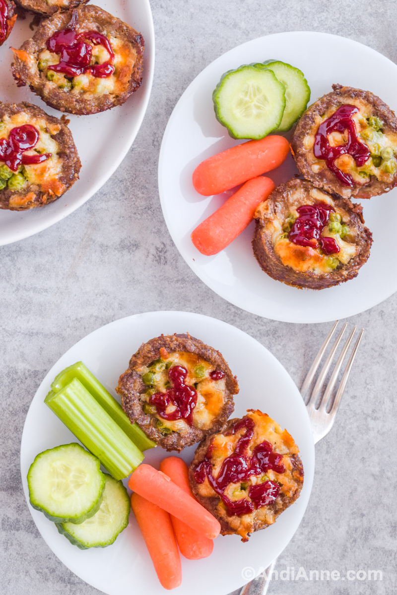 Set of two white plates with two meatloaf muffins, carrots and cucumber and a fork.