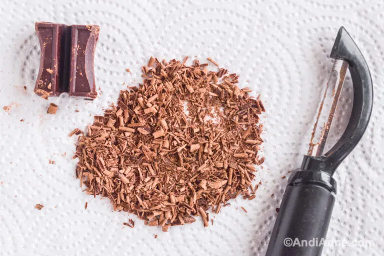 Chocolate shavings, a vegetable peeler and baker's chocolate square.