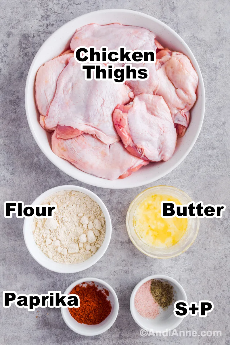 Recipe ingredients on counter including bowl of raw chicken, bowl of flour, melted butter, paprika, salt and pepper.