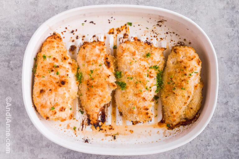 Four baked and breaded chicken breasts in a white casserole dish.