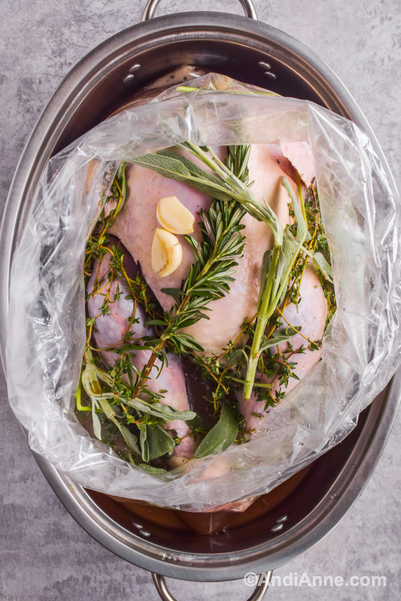 Raw turkey in a bag with fresh rosemary, sage, thyme and garlic. Sitting in a roasting pan.