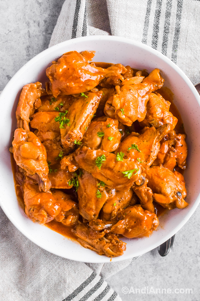 A white bowl with saucy barbecue ranch chicken wings piled inside. 