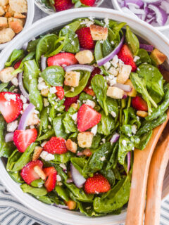 A bowl with spinach strawberry salad and wood spoons.