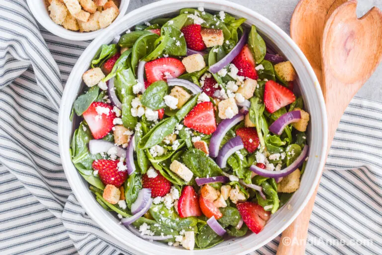 Strawberry spinach salad in a white bowl with wood spoons beside.