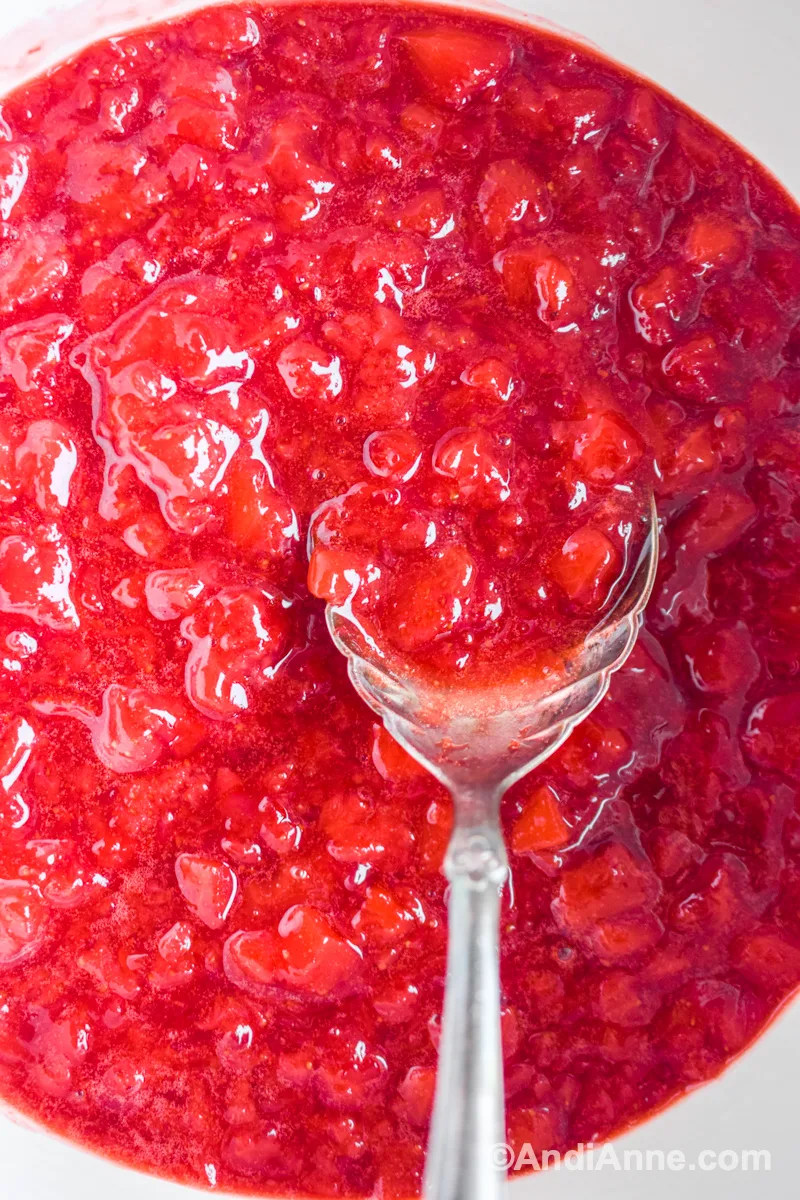 Close up of strawberry sauce with a large silver serving spoon inside.