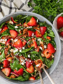 A big bowl of strawberry spinach salad topped with feta and crumbled bacon