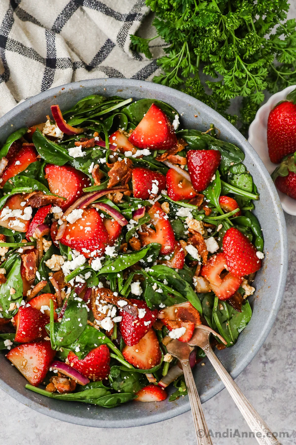 Close up of colorful strawberry spinach salad with sliced onion, crumbled feta and bacon.