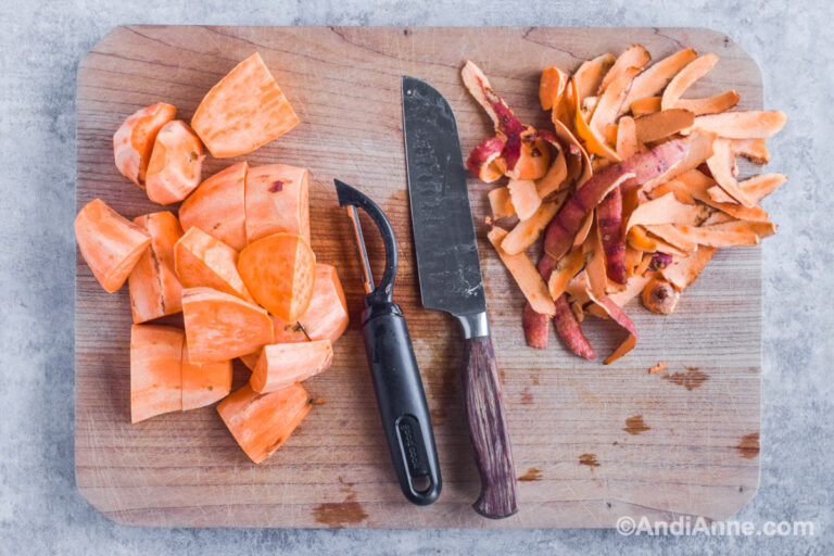 Chopped sweet potato on cutting board with knife, vegetable peeler and potato scraps.