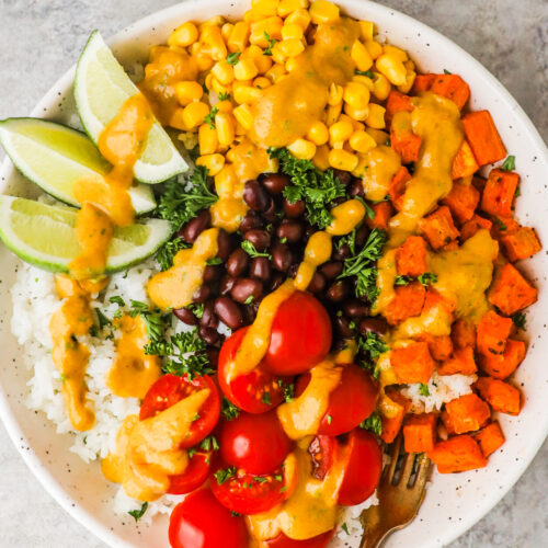 A bowl of sweet potato taco bowl with corn, black beanasm cherry tomatoes, limes and rice.